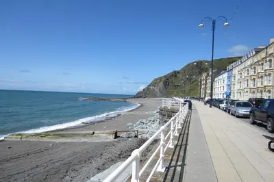 a beach with parked cars and buildings and the ocean at The Glengower in Aberystwyth