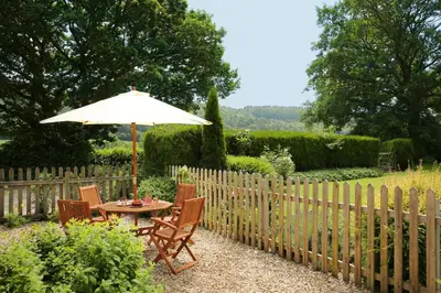 a table and chairs with an umbrella in a garden at Pheasant Walk at Eaton Manor in Church Stretton