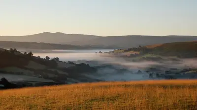 a foggy valley in the hills with a field at Barn Cottage in Brecon