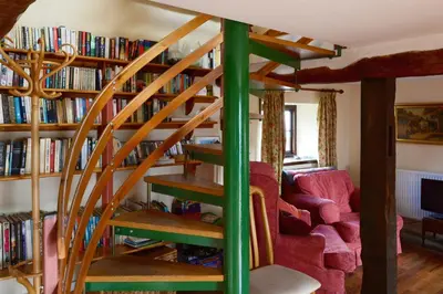 a wooden spiral staircase in a living room with bookshelves at Barn Cottage in Brecon