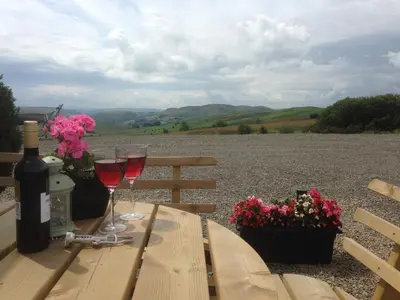 a wooden table with two glasses of wine and flowers at Upper Gilwern Quarry Hut in Llandrindod Wells