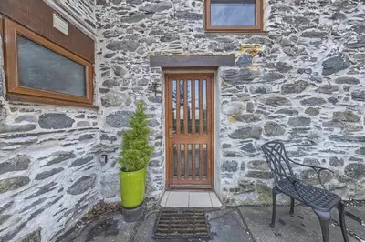 a stone building with a door and a chair and a plant at Beautiful 16th Century Ty Cerrig Cottage, set in stunning grounds with great views in Corwen