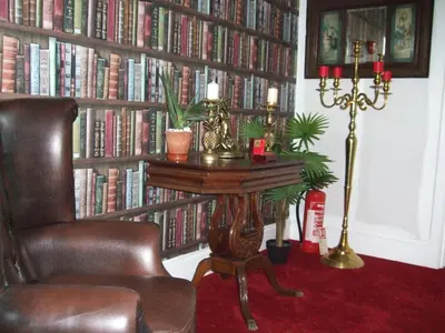 a room with a chair and a table and a book shelf with books at Bluebells guest house in Barmouth
