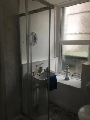 a bathroom with a shower with a sink and a window at Bluebells guest house in Barmouth