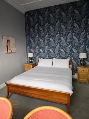 a bed in a room with two chairs and a wall at Bluebells guest house in Barmouth
