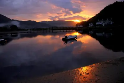 a person sitting on a boat in the water at sunset at George III Hotel in Penmaenpool