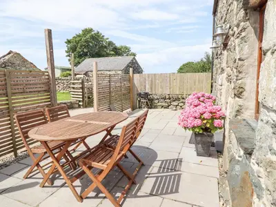 a wooden table and chairs on a patio with flowers at Isallt in Llanbedr