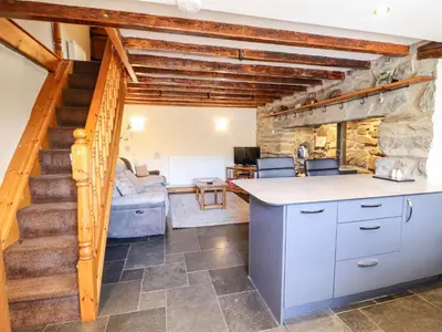 a kitchen with a staircase and a living room at Cwm Yr Afon Cottage in Harlech
