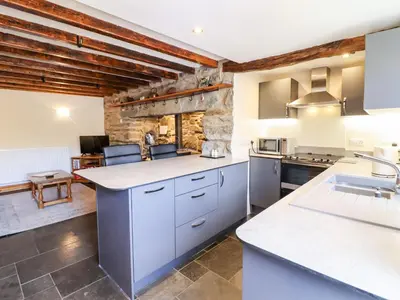 a kitchen with white cabinets and a stone wall at Cwm Yr Afon Cottage in Harlech