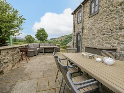 a patio with a wooden table and chairs at Byrdir Cottage in Llanwrthwl