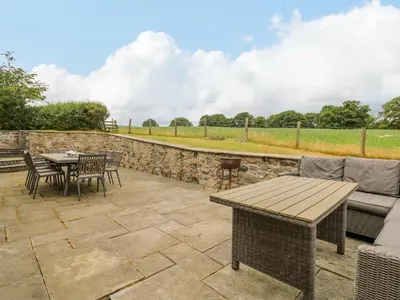 a patio with a table and chairs and a stone wall at Byrdir Cottage in Llanwrthwl