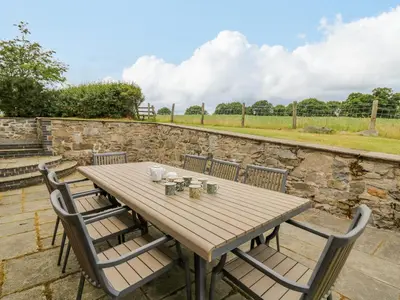 a wooden table with chairs and a stone wall at Byrdir Cottage in Llanwrthwl