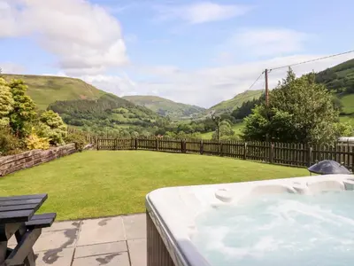 a hot tub with a view of a yard at Ysgubor Pwlliago in Pennant-Melangell