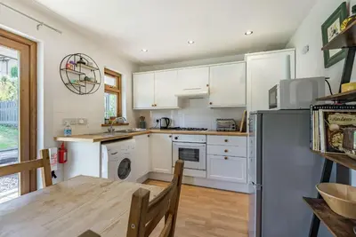 a kitchen with white cabinets and a table and a refrigerator at Gorwel in Blaenau-Ffestiniog