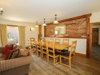 a dining room with a wooden table and a brick wall at Trooper's Barn in Acton Scott