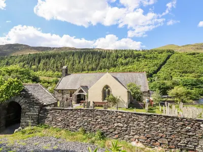 an old stone house with a stone wall at St Mary's in Tal-y-llyn