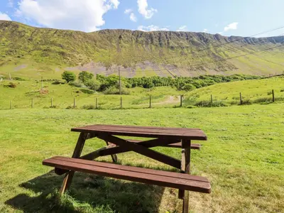 a wooden picnic table in a field with a mountain at St Mary's in Tal-y-llyn