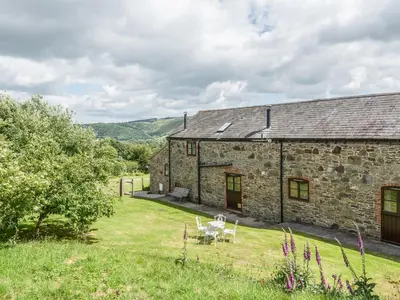 an old stone barn with two tables and chairs in a yard at Hope Hall Barn in Bromlow