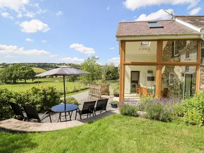 a house with a table and chairs and an umbrella at Llety'r Wennol in Llanycrwys