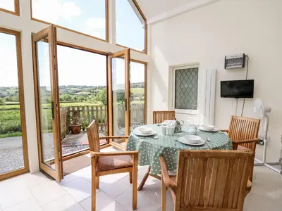 a dining room with a table and chairs and a television at Llety'r Wennol in Llanycrwys