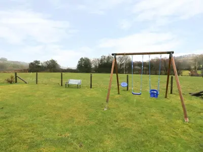 a swing set in a field with a bench at Tangaer Cottage in Cellan