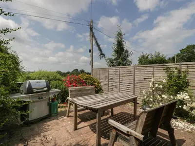 a picnic table and two chairs in a garden at Wheelbarrow Cottage in Stoke Prior