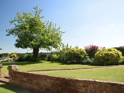 a brick retaining wall with a tree in a yard at Parrs Meadow Cottage in Pitchford