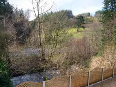 a fence next to a river in a field at Forestry Cottage in Pale
