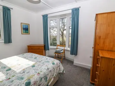 a bedroom with a bed and a chair and windows at Bron Aber in Arthog