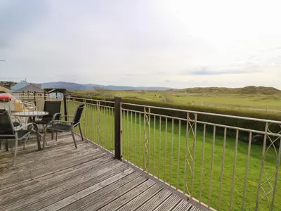 a deck with a table and chairs and a view of a field at Ty'r Heulwen in Aberdyfi