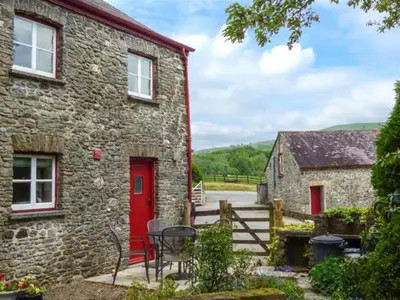 a stone house with a red door and a table and chairs at Crud-y-Barcud in Pumpsaint