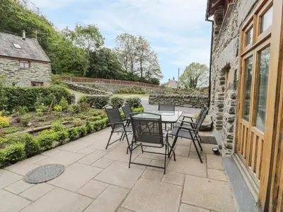 a patio with a table and chairs next to a building at Hendoll Barn in Fairbourne