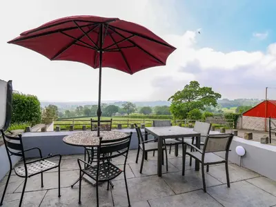 a patio with a table and chairs and an umbrella at Aberdauddwr in Llanwnen