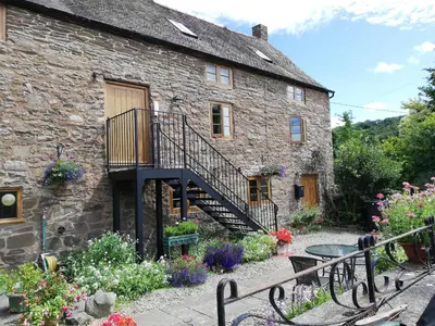a stone house with a staircase and flowers in front of it at The Barley Store in Craven Arms