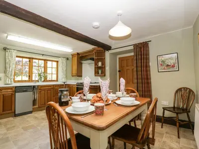 a kitchen with a wooden table with chairs and a dining room at Lower Court Byre in Kinsham