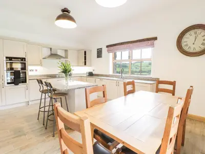 a kitchen with a wooden table and a clock on the wall at Sgubor in Llangwm