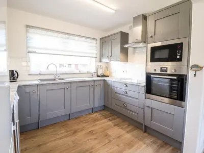 a kitchen with gray cabinets and a sink and a window at Sealyons in Fairbourne