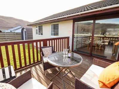 a wooden deck with a glass table and chairs at Sealyons in Fairbourne