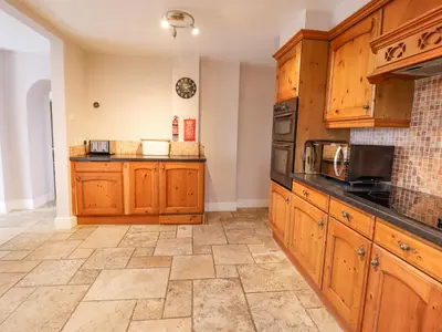 a kitchen with wooden cabinets and a tile floor at Is Y Deri in Harlech