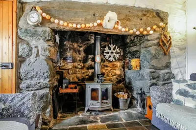 a stone fireplace in a room with a stove at Hwylfa'r Groes in Dyffryn