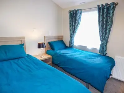 two beds in a bedroom with blue sheets and a window at Clearview Lodge in Borth