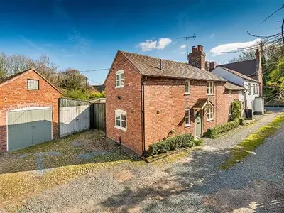 a red brick house with a garage on a street at Borrowers Cottage in Condover