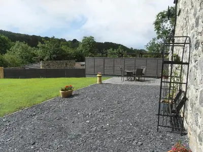 a garden with a patio with a table and a fence at Y Bwythyn at Henfaes in Rhydymain