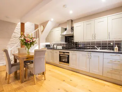 a kitchen with white cabinets and a wooden table with chairs at Moelfre Cottage in Llanbedr