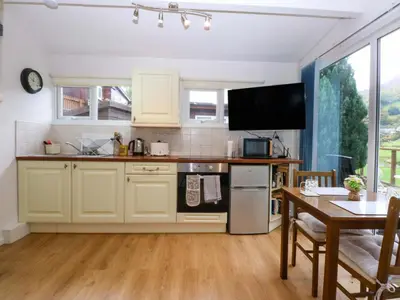 a kitchen with white cabinets and a table and a dining room at River's Nook in Llangynog