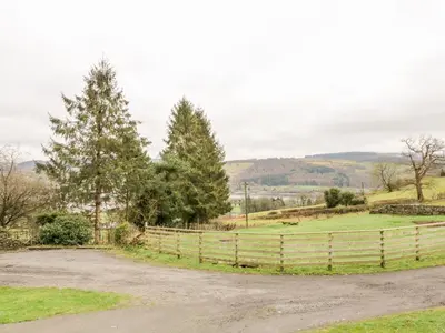a fence in front of a field with trees at Hen Ysgubor Cottage in Bala