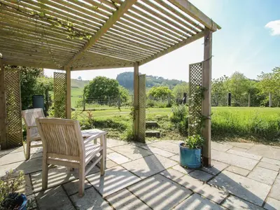 a pergola with two chairs and a table on a patio at The Old Beams at Pont y Forwyn in Llansantffraid-ym-Mechain