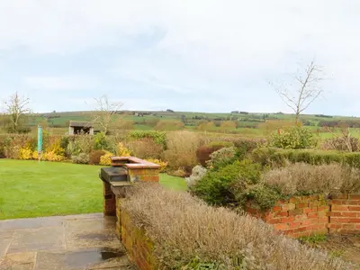 a garden with a brick wall and bushes at Ryelands Cottage in Easthope