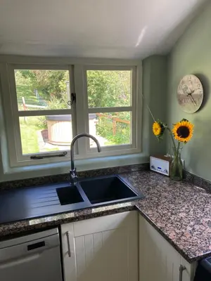 a kitchen counter with a sink and two windows at Riverside Cottage in Llangollen
