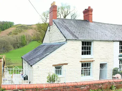 a white house with a roof and a fence at Riverside Cottage in Llangollen